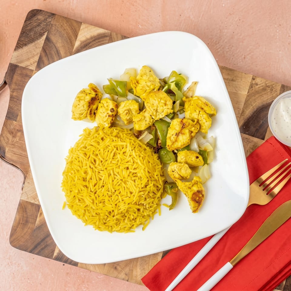 Chicken and peppers with yellow rice on a white plate, with a red napkin and gold cutlery.
