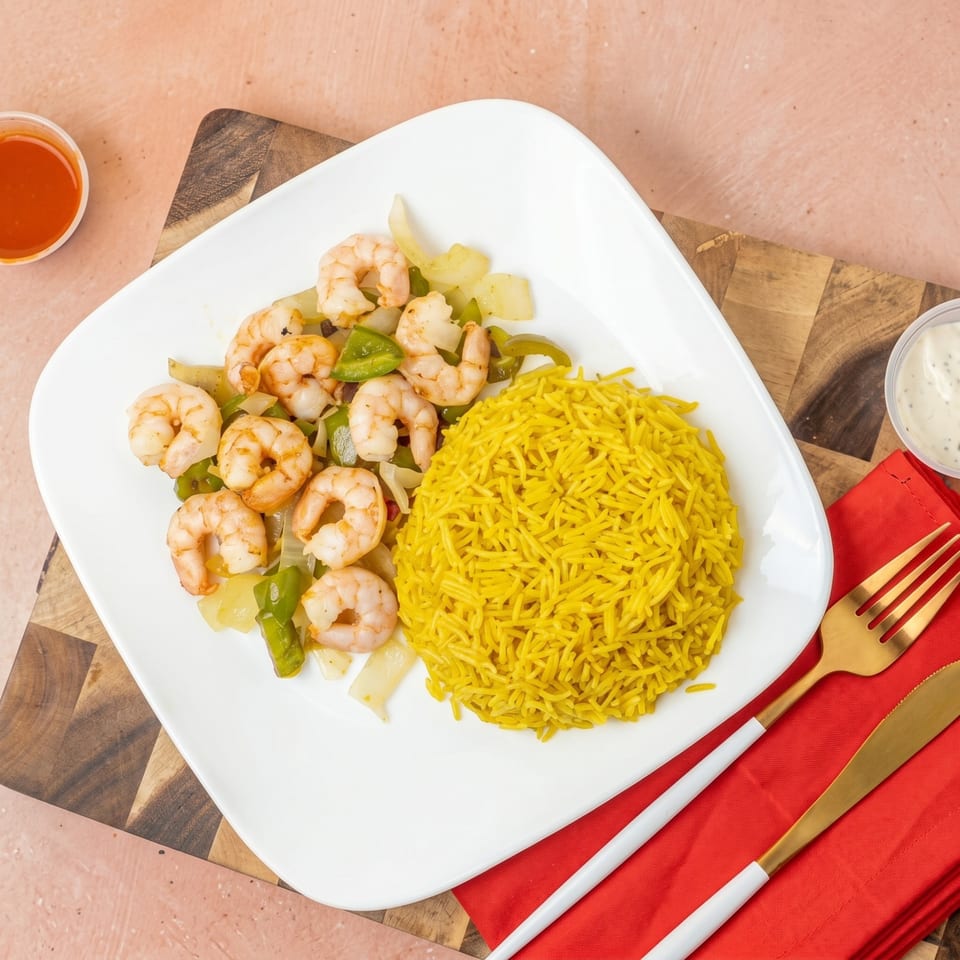 Shrimp stir-fry with green peppers and onions, alongside yellow rice, on a white plate.