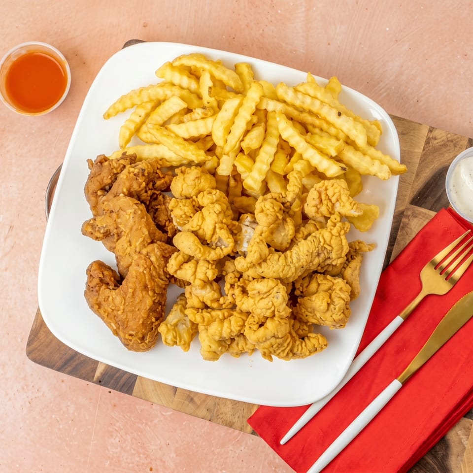 Crispy fried chicken wings, chicken tenders, and crinkle-cut fries on a white plate with dipping sauces.