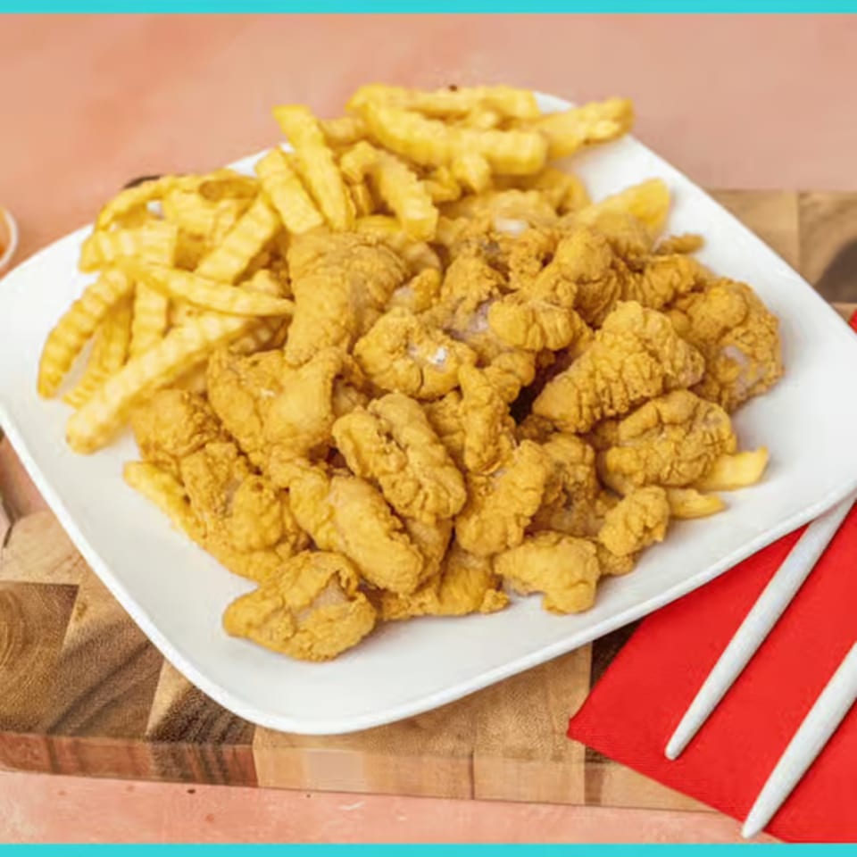 A white plate holds crispy fried chicken pieces and crinkle-cut french fries, with chopsticks on a red napkin.