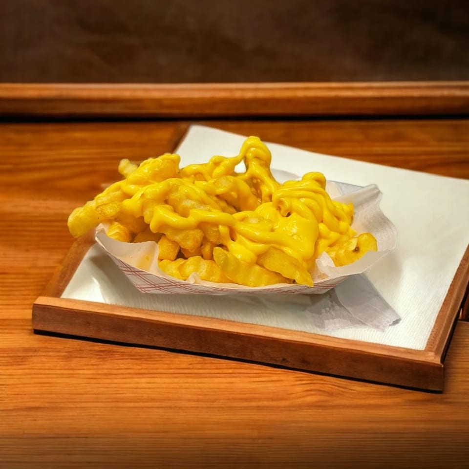 A paper boat of Snappers' golden waffle fries, generously topped with melted cheese sauce, on a wooden tray.
