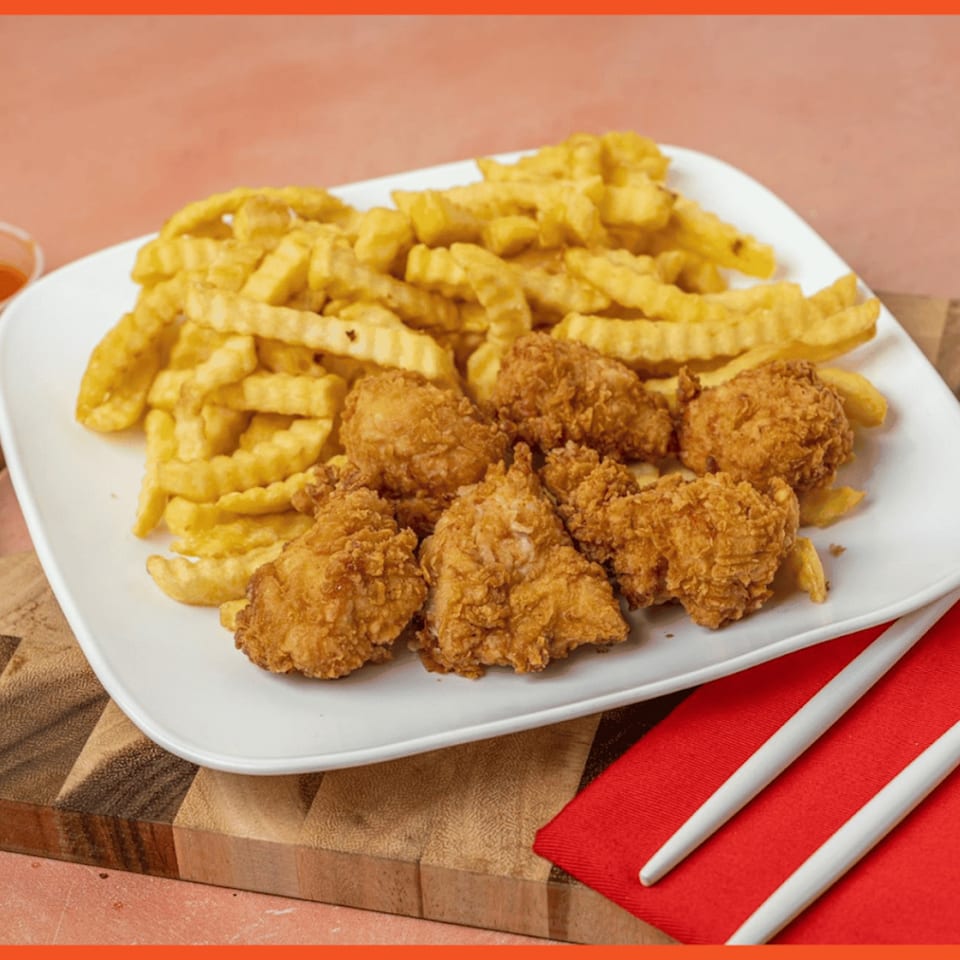 A white plate with golden-brown fried chicken pieces and crinkle-cut fries on a wooden board.