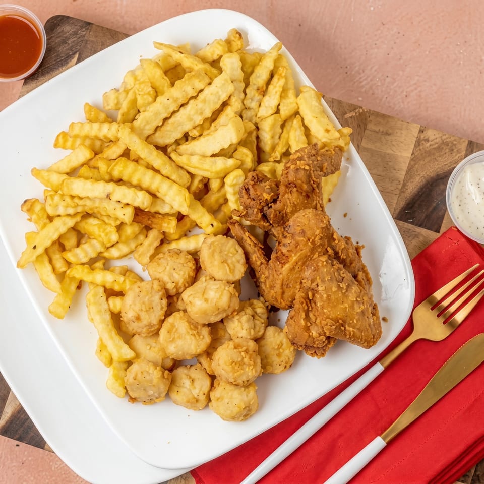 A white plate filled with golden french fries, crispy fried chicken wings, and popcorn chicken.